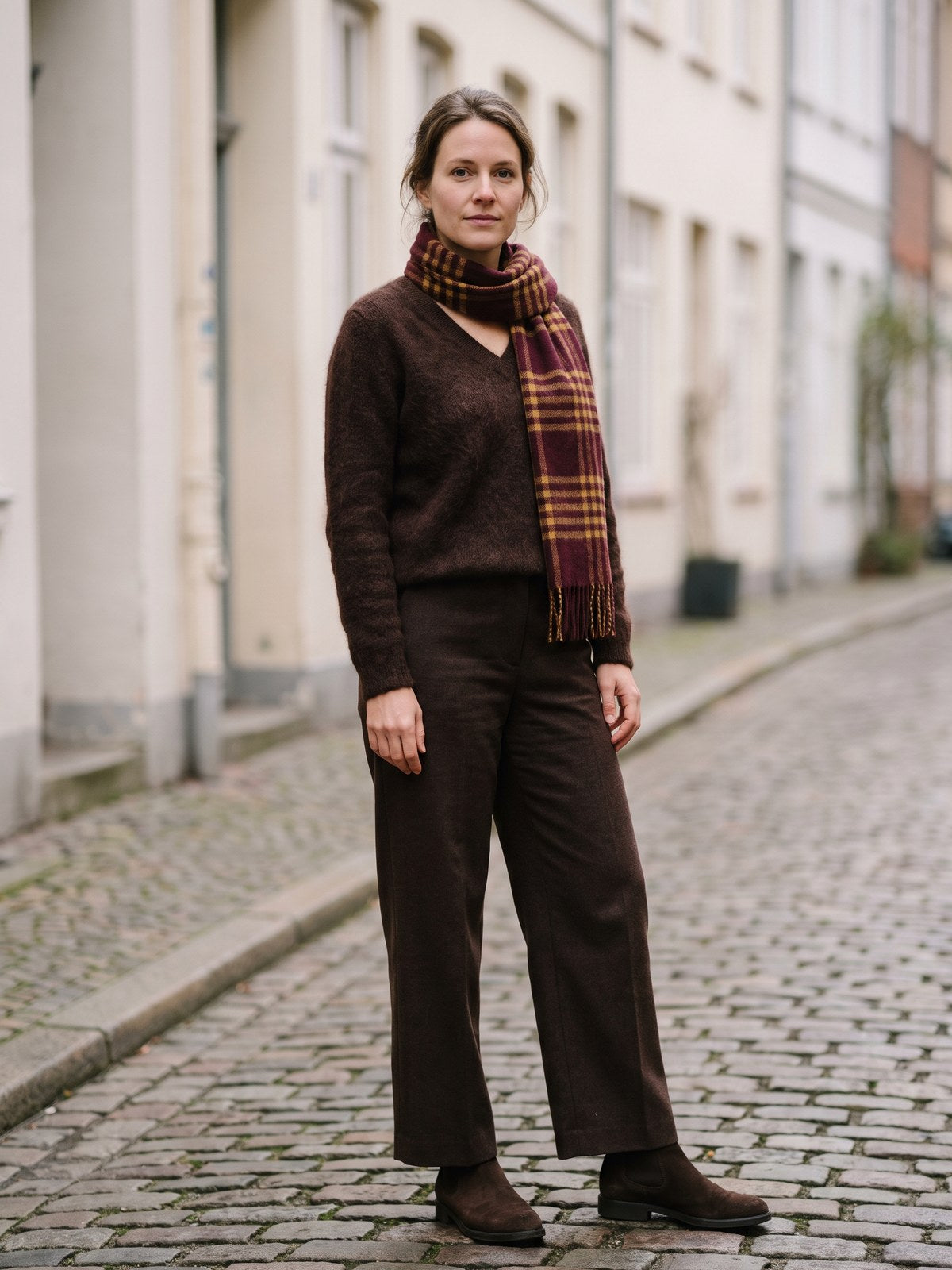 Frau in braunem Alpaka-Pullover, brauner Wollhose und braunen Wildleder-Chelsea-Boots mit kariertem Schal