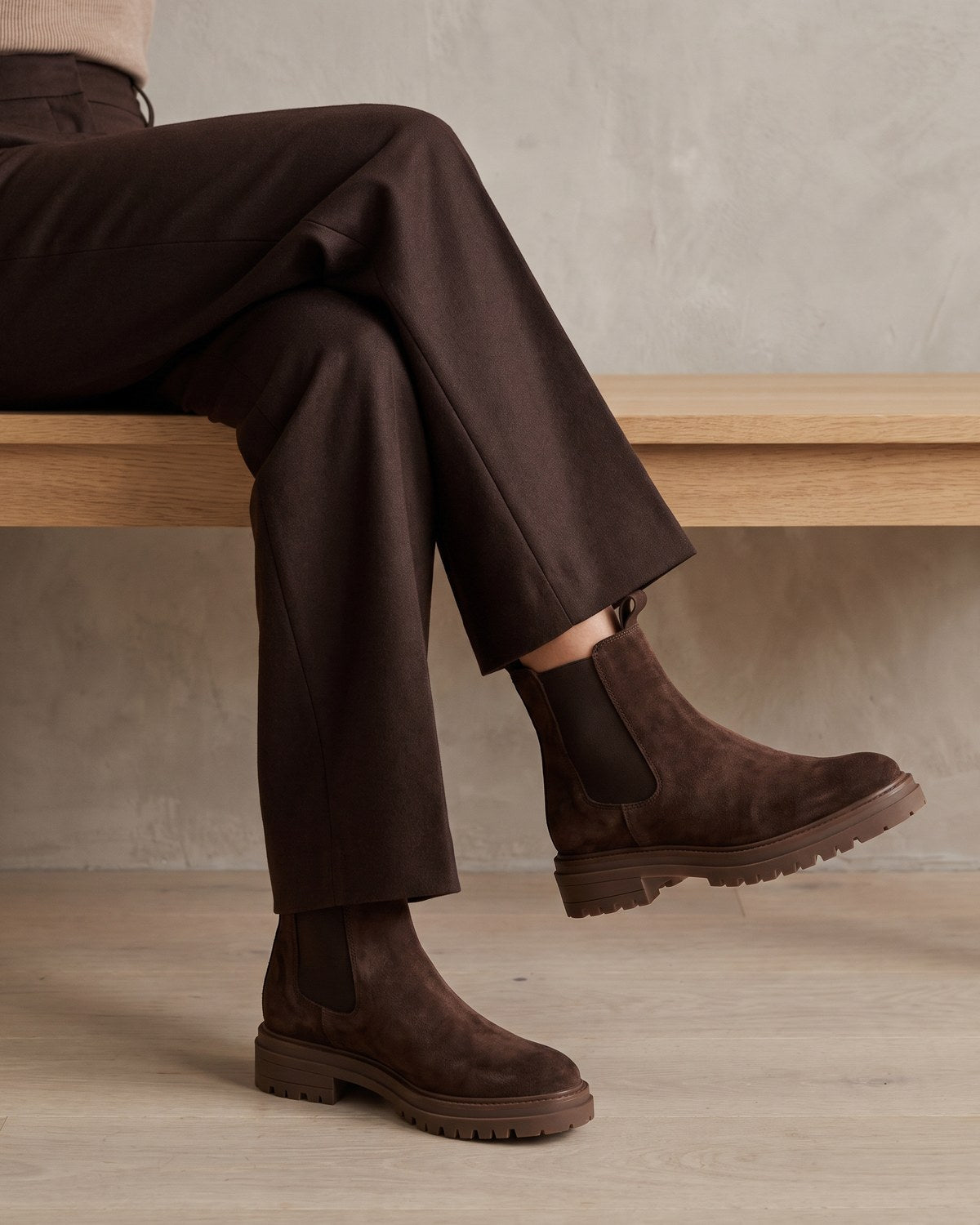 Braune Wildleder-Chelsea-Boots zu brauner Wollhose, sitzend auf einer Holzbank